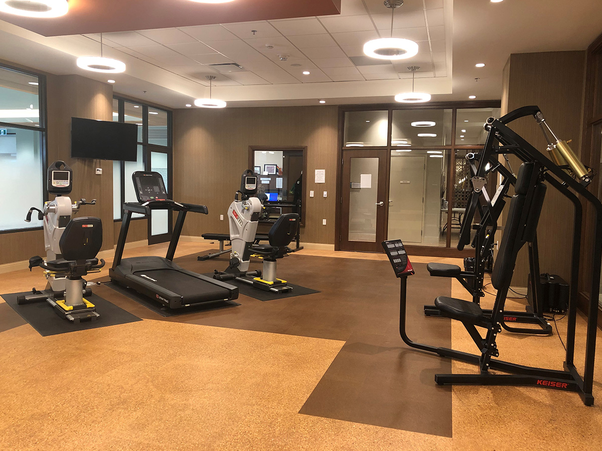 Empty fitness room with a weight machine in front and a treadmill and TV behind.