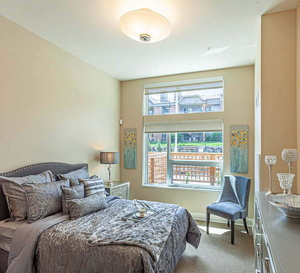 Bedroom with a gray upholstered bed in front and dresser with decor behind, window between them.