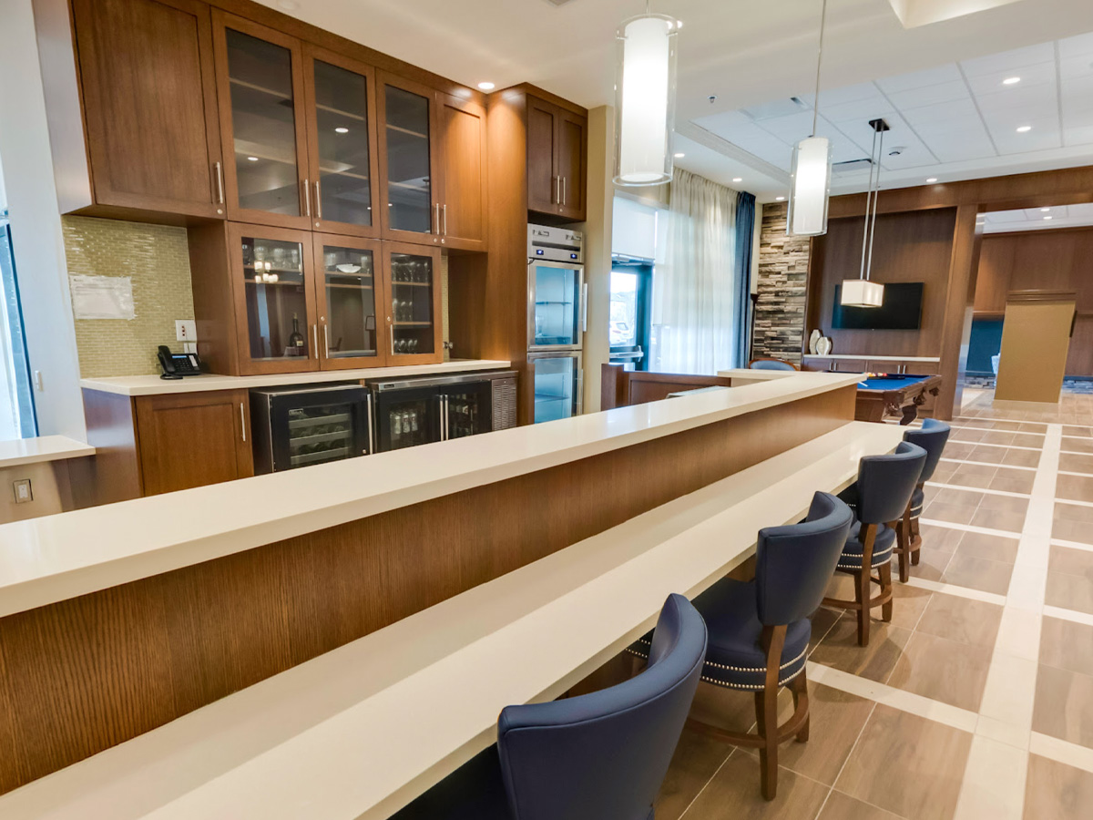 Bar area with blue stools in front, wine coolers and cabinets behind, pool table visible in the back.